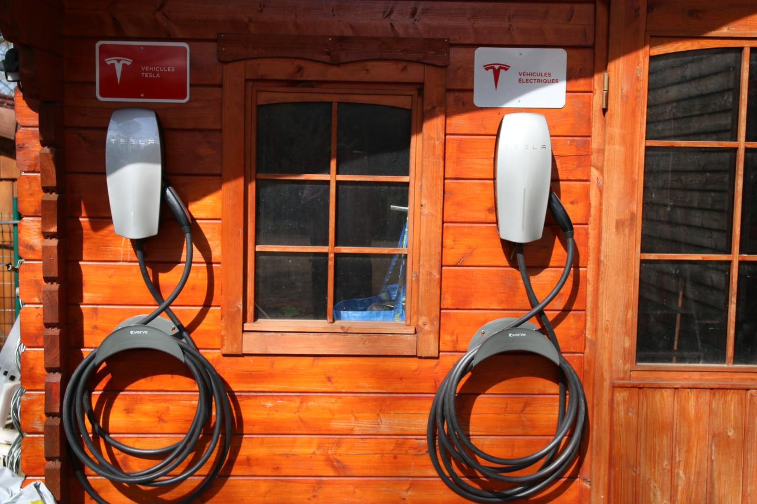 A wooden cabin with two Tesla charging stations and a window.