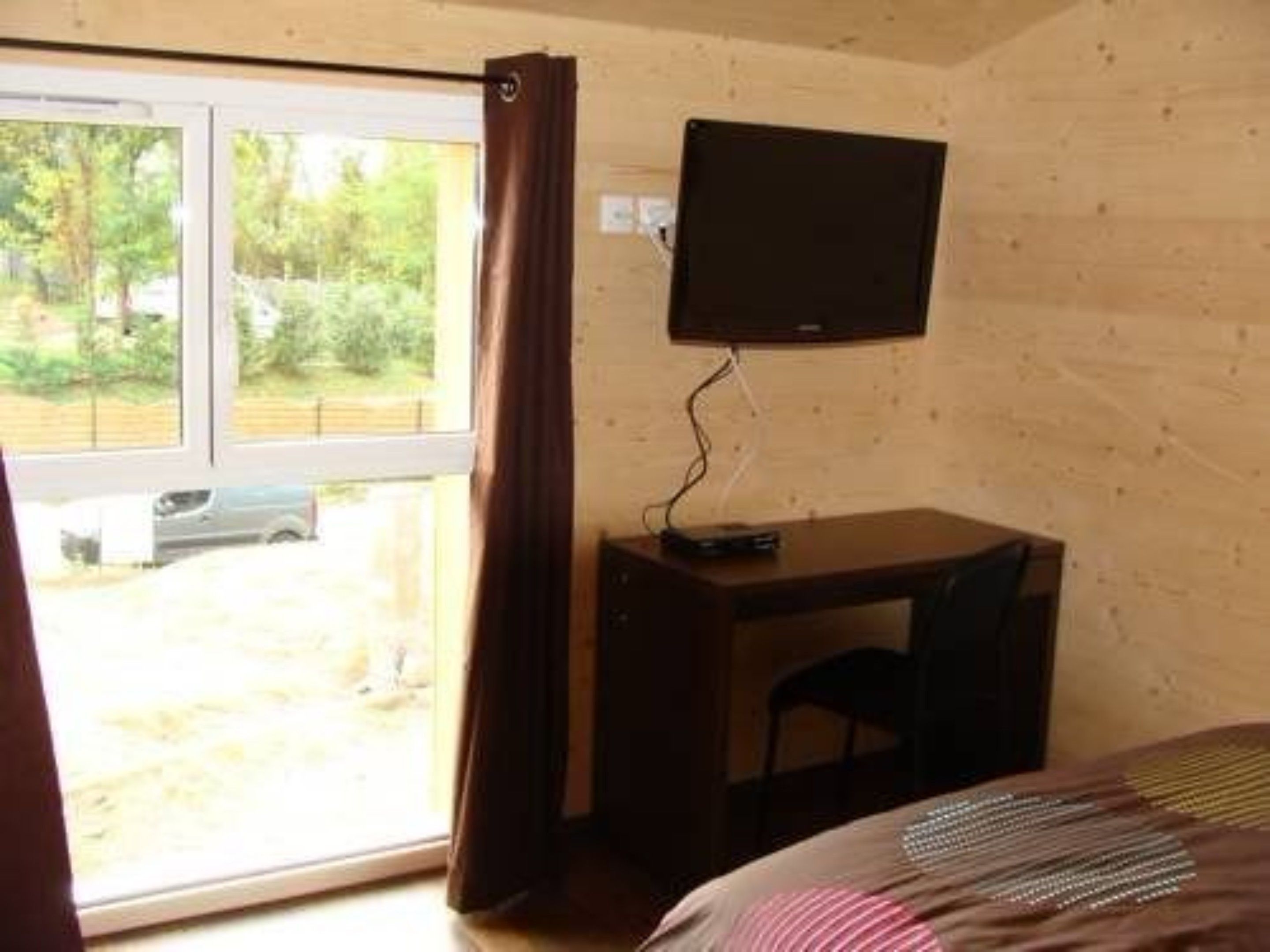 Una habitación con cama, escritorio, silla, televisor montado en la pared y ventana con cortinas.