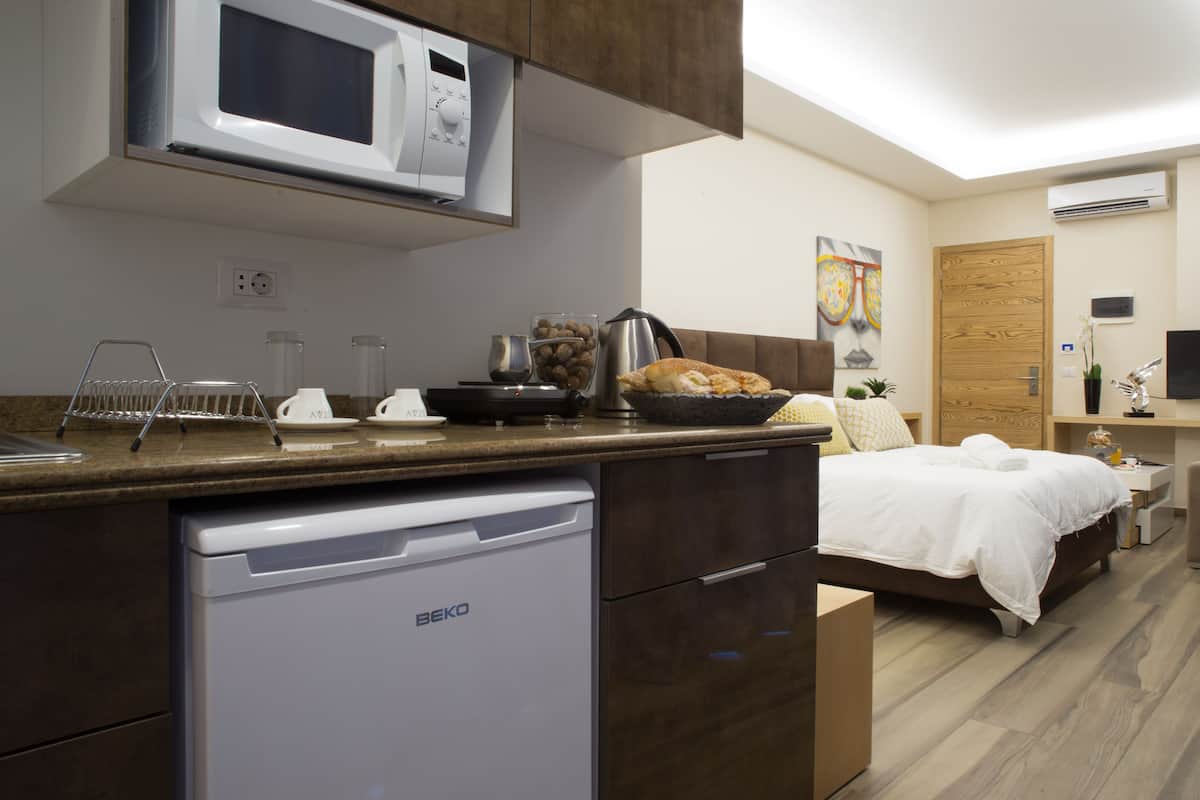 Eine moderne Küche mit Mikrowelle, Kaffeemaschine und Spüle. Ein Bett mit Fernseher und eine kleine Sitzecke sind ebenfalls vorhanden.