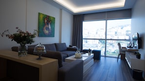A modern living room with a sofa, a coffee table, a vase with flowers, a painting, and a large window with a city view. - The Stay Furnished Apartments (Dbayeh)