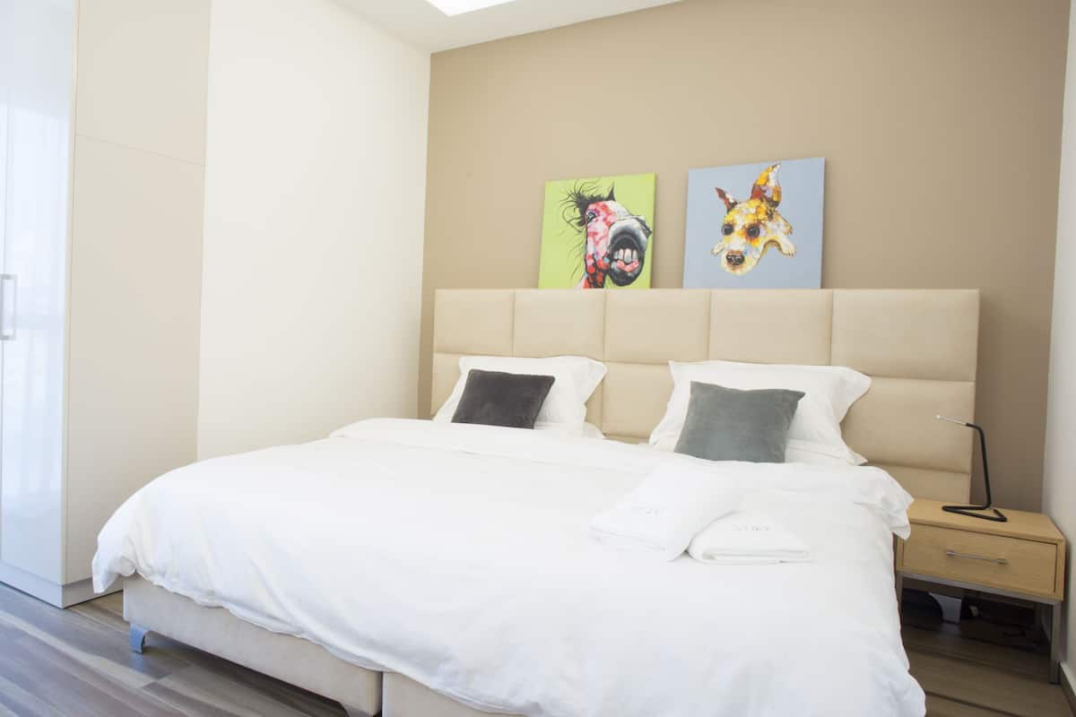Ein modernes Hotelzimmer mit einem großen Bett, zwei Kissen, einem Nachttisch mit Lampe und einem Bild an der Wand.