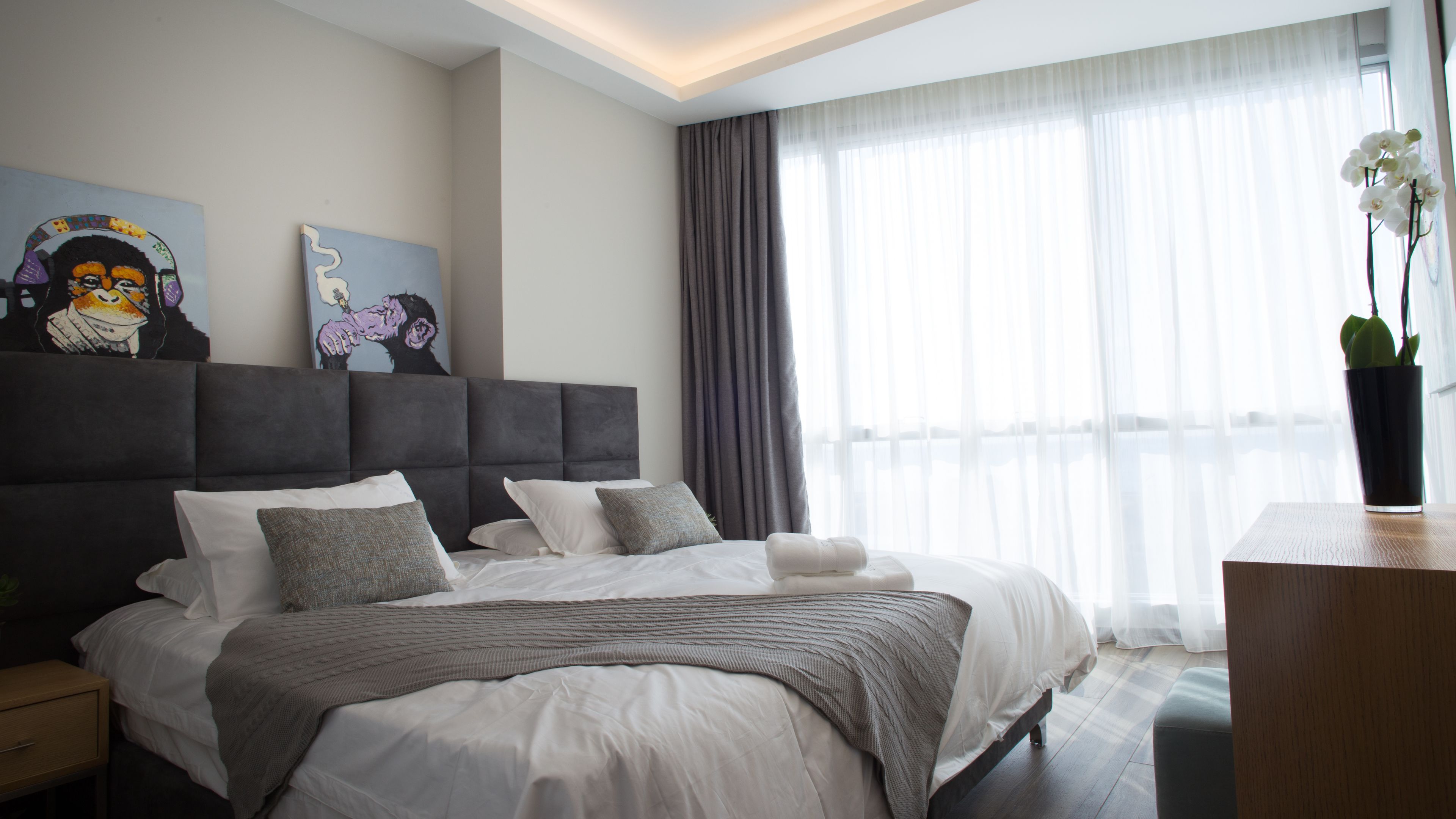 Um quarto de hotel moderno com uma cama grande, cortinas cinzas e obras de arte na parede.