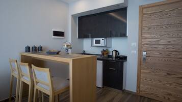 A compact kitchen with a wooden table, two chairs, a microwave, a kettle, and a small sink.