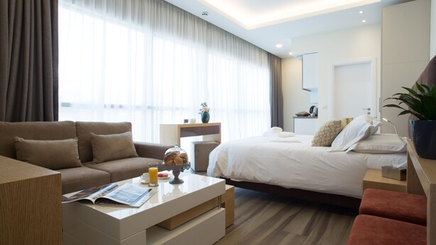 A modern hotel room with a large bed, a sofa, a coffee table with a magazine, and a small table with a vase and a plant. - The Stay Furnished Apartments (Dbayeh)
