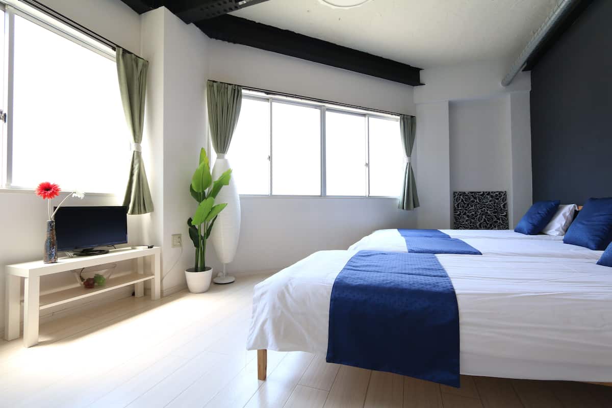 Ein modernes Hotelzimmer mit einem großen Bett, einem Fernseher auf einer weißen Ablage, einer Zimmerpflanze und einem Fenster mit Vorhängen.