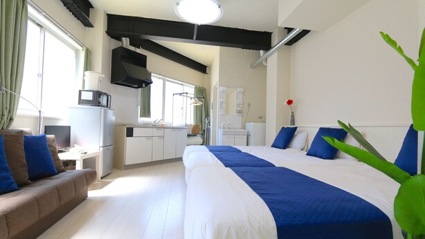 Quarto de hotel moderno com cama grande, sofá, cozinha compacta e banheiro.
