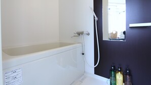 Casa de banho com banheira, janela e três frascos de produtos de higiene no balcão.