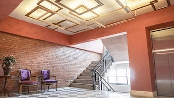 Un hall con suelo a cuadros, dos sillas moradas, una pared de ladrillo y una escalera.