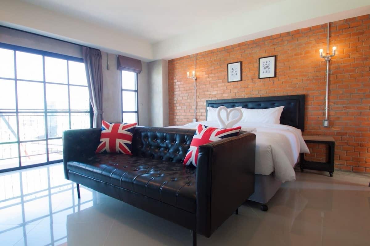 Une chambre d’hôtel avec un canapé en cuir noir, un lit avec une literie blanche, un mur en briques et deux lampes fixées au mur.