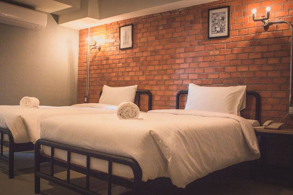 Une chambre d’hôtel avec deux lits, un mur en briques et une table de chevet avec une lampe.