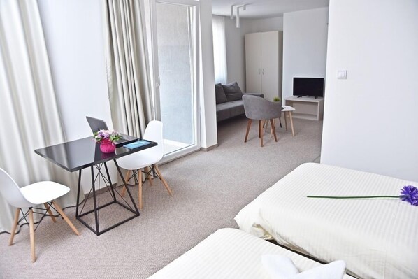 A modern hotel room with a bed, a desk with a laptop, a chair, a sofa, and a TV.