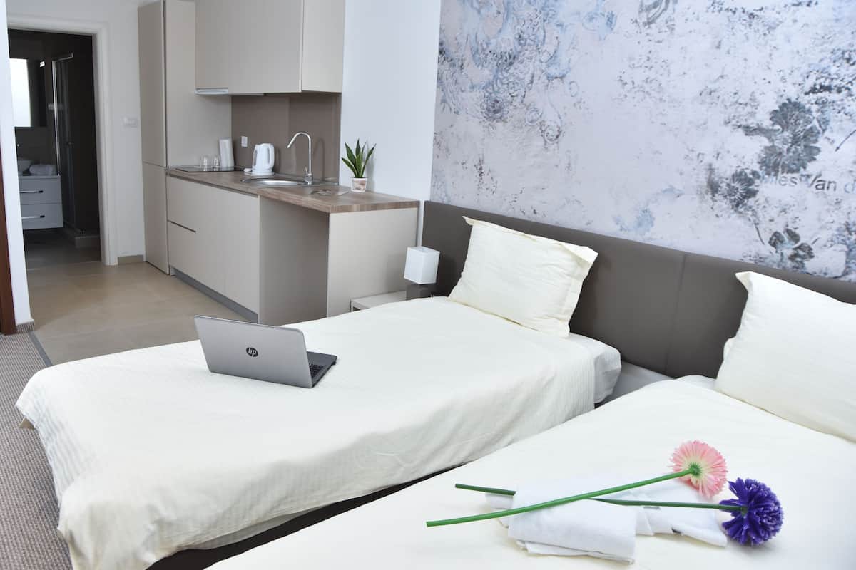 A hotel room with a bed, a desk with a laptop, a sink, and a plant.