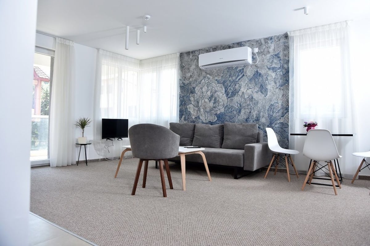 A modern living room with a grey sofa, white chairs, a flat-screen TV, and a patterned wall.