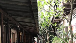 Un sendero estrecho bordeado por construcciones de madera y exuberante vegetación, que conduce a la entrada de un edificio.