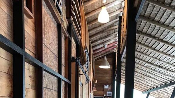 Un pasillo con paredes y suelo de madera, que conduce a una zona de estar con bancos y mesas.