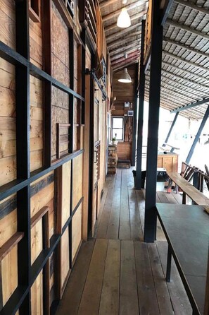 A corridor with wooden walls and a wooden floor, leading to a seating area with benches and tables. - Cafe Del Sunshine - Hostel (Ko Chang)