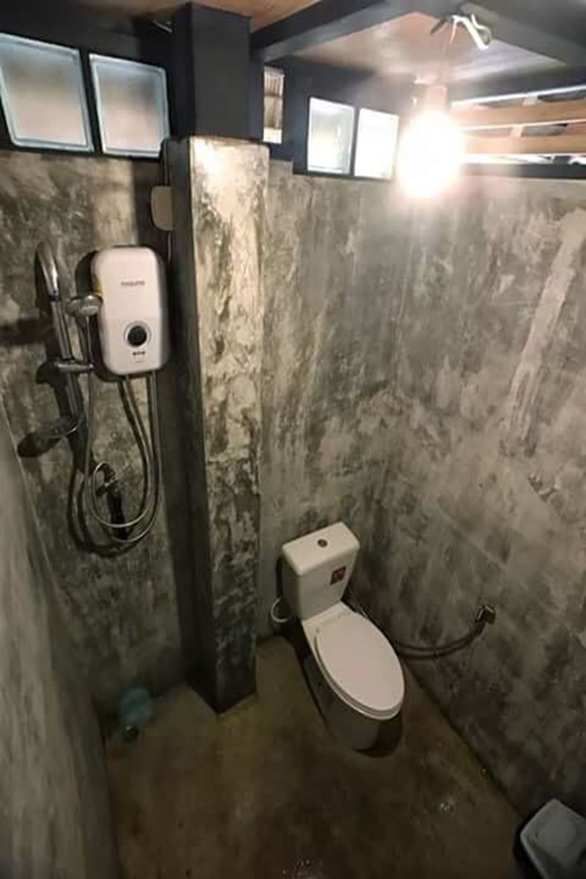 A compact bathroom with a toilet, a handheld showerhead, and a soap dispenser.