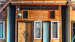 Una cabaña de madera con una puerta grande, dos ventanas y una hamaca en el porche.