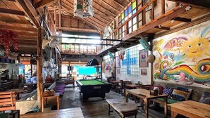 Un interior rústico de madera con mesa de billar, bancos y un mural.