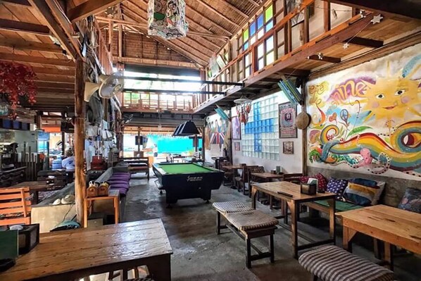 Un interior rústico de madera con mesa de billar, bancos y un mural.