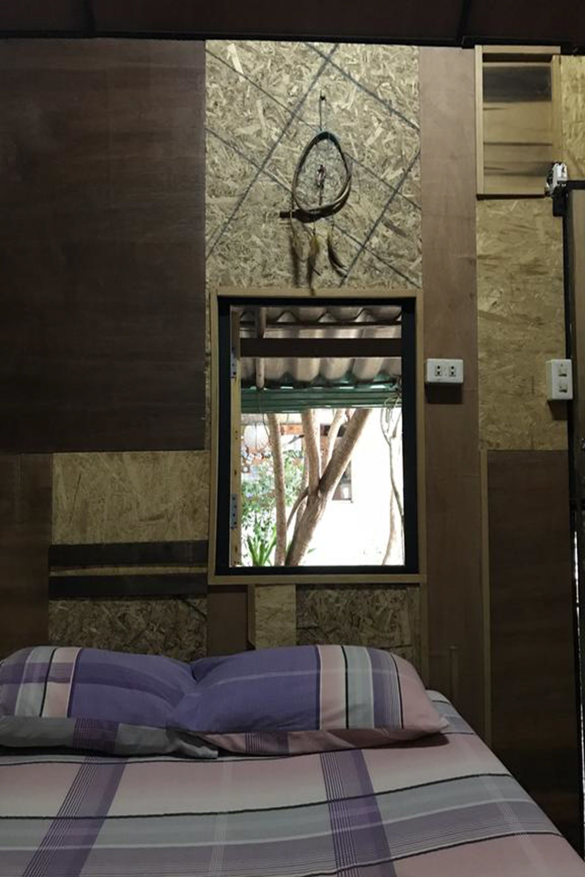A bedroom with a bed, a window with a view of trees, and a wall-mounted dreamcatcher.