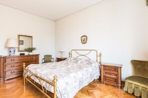 A bedroom with a bed, wooden dresser, nightstand, chair, and a mirror on the wall.