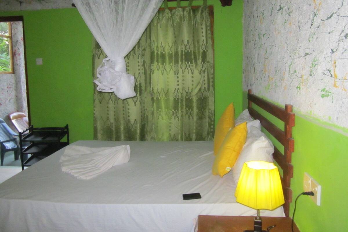 A bed with white bedding, a yellow lamp, and a mobile phone on the bedside table.