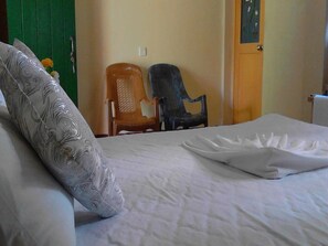 A bed with a white bedspread and a decorative pillow, two chairs, a green door, and a wall with a light switch. - Sigiriya Vee Guest (Sigiriya)