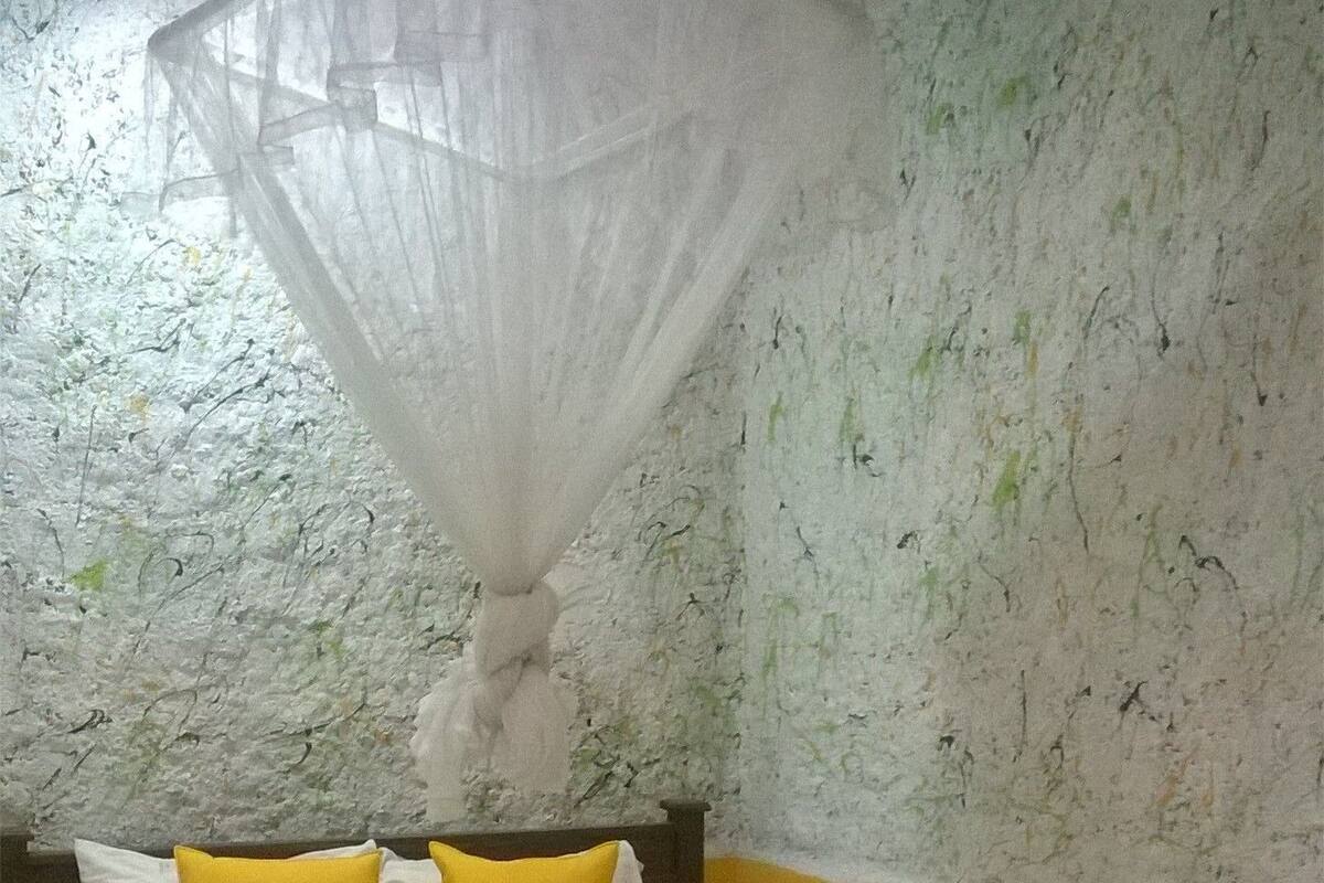 A bed with a canopy, yellow pillows, and a white bedspread in a room with textured walls.
