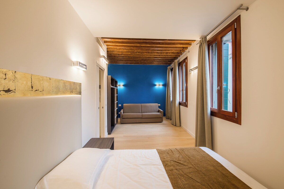Un pasillo estrecho que conduce a un dormitorio con cama, sofá y una pared azul.