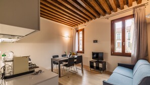 A modern living room with a wooden ceiling, a dining area with a table and chairs, a sofa, a TV, and a kitchen area with a stove and a coffee machine. - Charming Palace Corte Del Teatro (Venice)