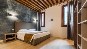 A bedroom with a large bed, wooden nightstand, and built-in shelving. - Charming Palace Corte Del Teatro (Venice)