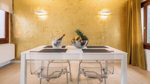 A dining area with a white table, two chairs, a fruit bowl, and a wall with a textured finish. - Charming Palace Corte Del Teatro (Venice)