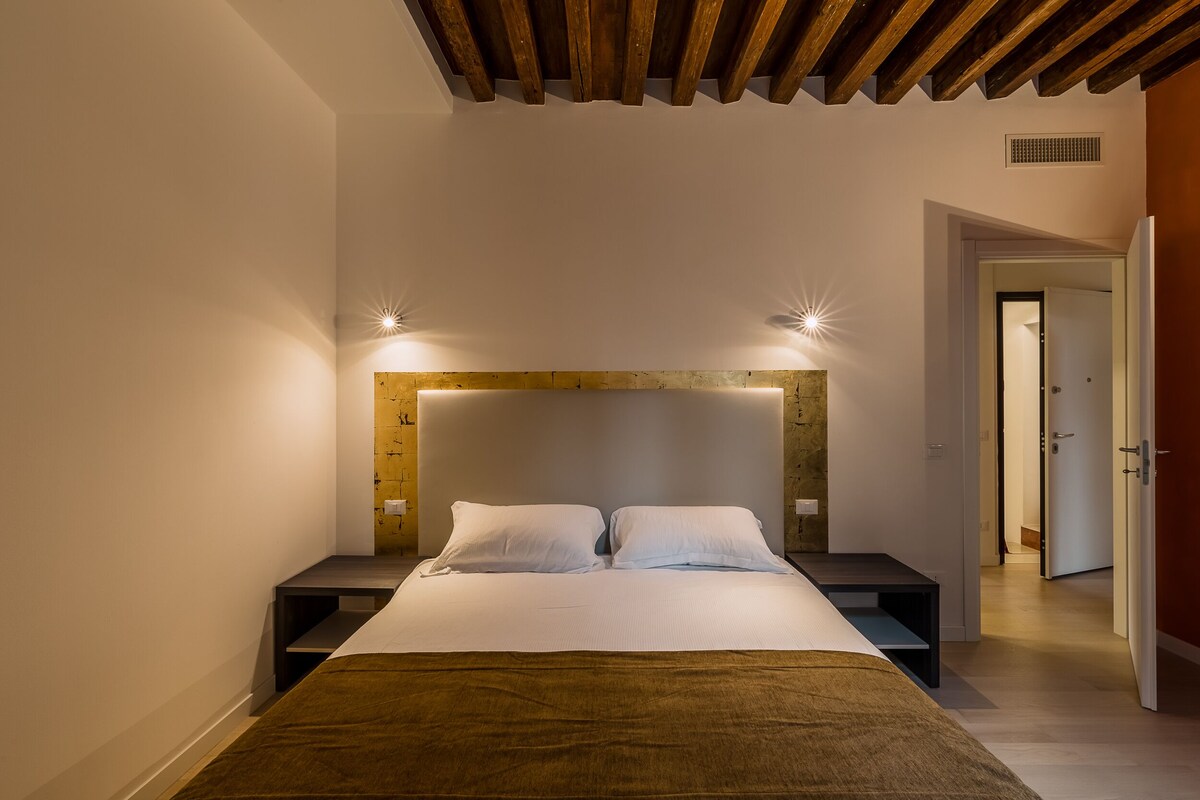 Un dormitorio moderno con cabecera de madera, dos mesitas de noche y una cama grande.