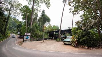 A roadside OYO hotel with a covered outdoor seating area and a parked car.