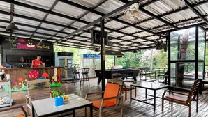 An outdoor dining area with wooden tables and chairs, a bar counter, and a view of the outdoors.
