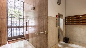 Entrada de un edificio moderno con una reja metálica, un detector de incendios y un buzón de correo.