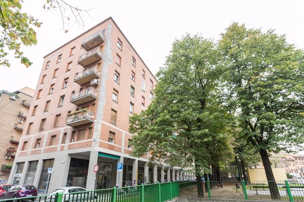 Un immeuble à plusieurs étages doté de balcons, d’un panneau indiquant un parking et d’un grand arbre à l’avant.