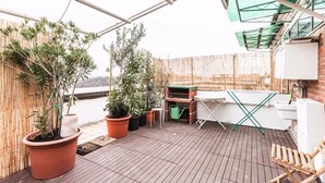 Una terraza en la azotea con macetas, una parrilla, una mesa plegable y una silla de madera.