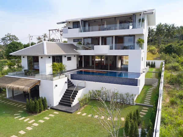 A modern multi-story house with a swimming pool, a staircase leading to the upper floor, and a well-maintained garden.