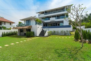 Una casa moderna de varios pisos con un césped bien cuidado, una escalera que lleva a la entrada y un pequeño patio.