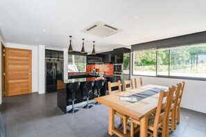 Una cocina moderna con una isla central, taburetes negros y un comedor con mesa y sillas de madera.