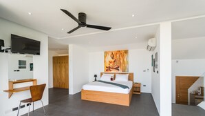 Une chambre à coucher moderne, comprenant un lit, un bureau, une chaise, un ventilateur de plafond et un tableau représentant une figure en méditation.