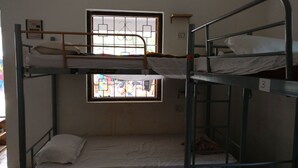 A dormitory room with bunk beds, a window with bars, and a small shelf. - Pappi Chulo Hostel (Vagator)