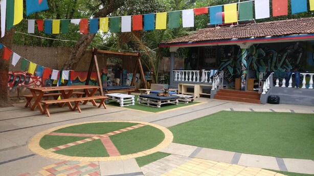 A courtyard with picnic tables, a stage, and colorful flags. - Pappi Chulo Hostel (Vagator)