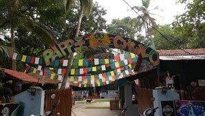 A hostel entrance with colorful flags, a wooden fence, and a dog in the foreground. - Pappi Chulo Hostel (Vagator)