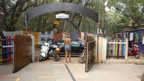 A hostel entrance with a signboard, a wooden gate, and a motorbike parked inside. - Pappi Chulo Hostel (Vagator)