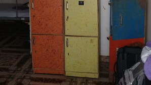 A room with a bed, a small table, a fan, and a cabinet with drawers. - Pappi Chulo Hostel (Vagator)