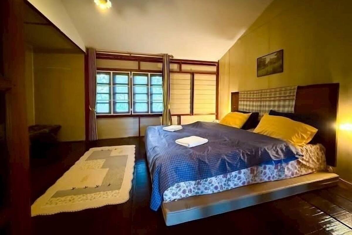 Un dormitorio con cama, mesita de noche, ventana con cortinas y lámpara colgante.