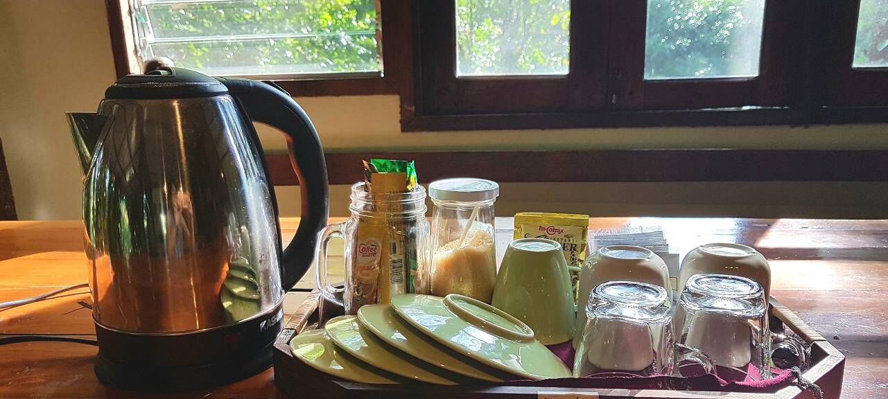 A kitchen area with a kettle, jars, plates, and a tray of glasses.